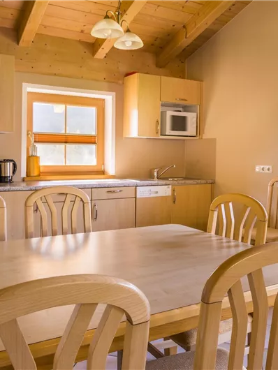 Een lichte en gezellige keuken met houten planken en een grote eettafel. Vensters laten veel licht binnen en de uitrusting is modern.