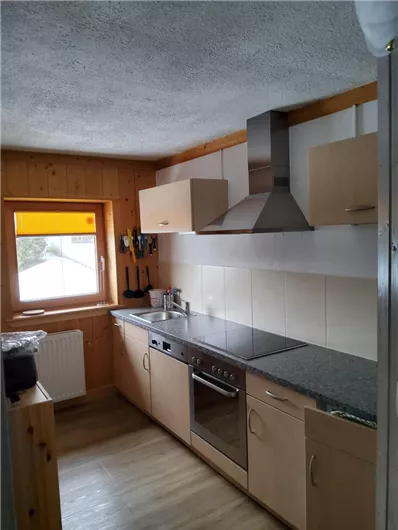 Eine moderne Küche mit Holzverkleidung und einem großen Fenster. Sie verfügt über einen Ofen, einen Kühlschrank und eine Kochstelle.