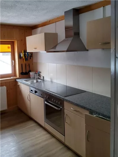 Eine moderne Küche mit hellen Oberflächen und einem integrierten Herd. Die Wände sind teilweise aus Holz, und die Fenster bringen viel Licht hinein.