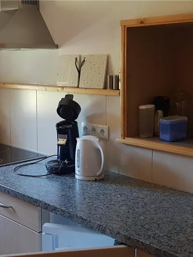 Eine moderne Küche mit grauem Granitboden und hellen Wänden. Sie enthält Kochgeräte, eine Kaffeemaschine und ein Fenster mit natürlichem Licht.