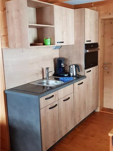 Eine moderne Küche mit Holzfronten und einem dunklen Arbeitsbereich. Sie ist ausgestattet mit einer Spüle, Kaffeemaschine und einem Backofen.