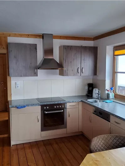 Eine moderne Küche mit Holzdetails und einem Essbereich. Die Ausstattung umfasst einen Herd, eine Spüle und Fenster mit Blick nach außen.