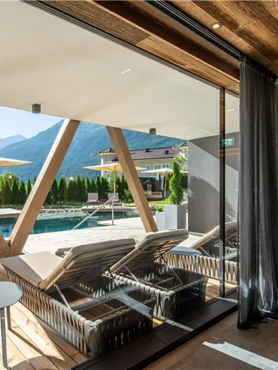 Innenansicht eines modernen Raumes mit Blick auf einen Pool und die Berge. Bequeme Liegen stehen bereit, um die Aussicht zu genießen.