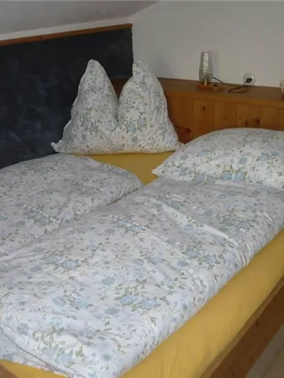 Ein gemütliches Schlafzimmer mit einem Holzbett und bunten Bettwäsche. Auf dem Bett liegen Kissen und eine zusätzliche Decke.