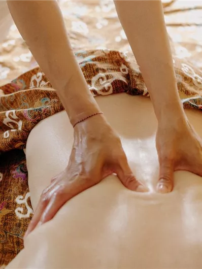 Eine Person liegt entspannt auf einer Liege, während eine andere Person eine Massage gibt. Der Hintergrund ist warm und einladend gestaltet.