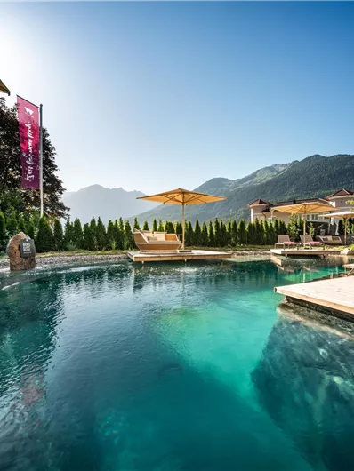 Ein schöner Pool umgeben von Bäumen und Bergen. Klare Himmel und Sonnenschirme laden zum Entspannen ein.