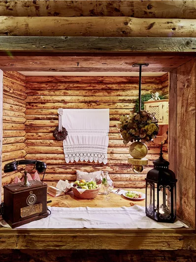 Een gezellig raam in een houten hut met rustieke decoratie. Op de tafel staan verse voedingsmiddelen en een lantaarn.