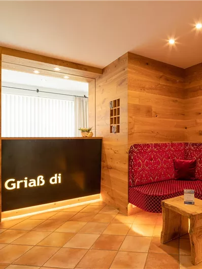 Ein einladender Empfangsbereich mit Holzwänden und warmer Beleuchtung. Rote Sitzbänke und eine dekorative Blumenarrangement schaffen eine gemütliche Atmosphäre.