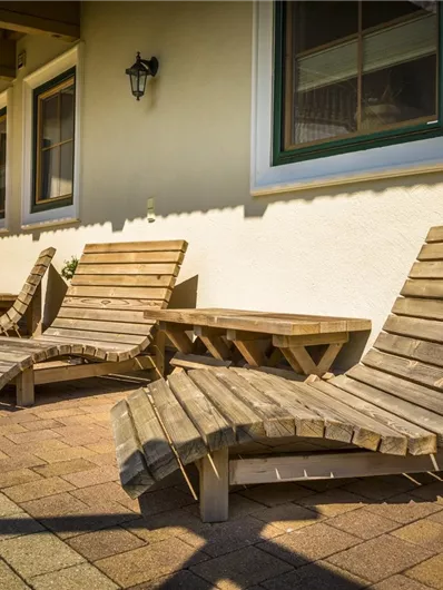Een hof met vier houten ligstoelen en een kleine tafel. De ligstoelen zijn in warm licht op een geplaveide vloer geplaatst.