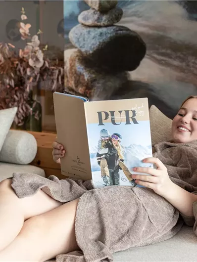 Drei Kinder in Bademänteln sitzen auf einer Couch und lesen zusammen ein Magazin. Sie lachen und genießen die gemeinsame Zeit.