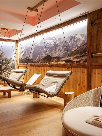 A relaxing wellness area with wooden decor and comfortable hanging loungers. In the background, an impressive mountain landscape.