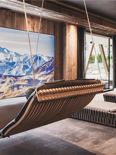 Ein modernes Zimmer mit einer hängenden Schaukel und einem großen Bild von schneebedeckten Bergen. Die Einrichtung ist aus Holz und sorgt für eine gemütliche Atmosphäre.