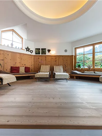 Ein ruhiger Entspannungsraum mit Holzverkleidung und großen Fenstern. Bequeme Liegen laden zum Relaxen ein.