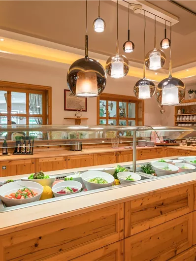 Eine moderne Küche mit Holzverkleidung und einem großen Buffet. Frische Salate und verschiedene Zutaten sind gut sichtbar.
