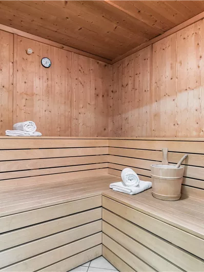 Eine gemütliche Sauna aus Holz mit Bänken und Handtüchern. Ein Eimer und eine Sanduhr sind ebenfalls vorhanden.