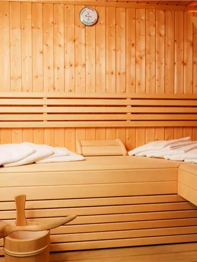 Eine gemütliche Sauna mit Holzwänden und Bänken. Auf den Liegen liegen Kissen und ein Thermometer zeigt die Temperatur an.