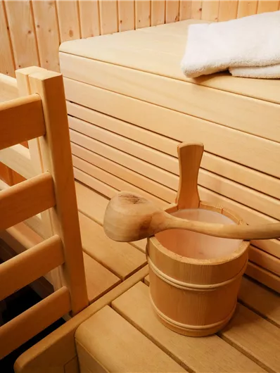 Eine gemütliche Sauna mit Holzbänken und einem kleinen Eimer. Auf der Bank liegen zwei Handtücher bereit für die Nutzung.