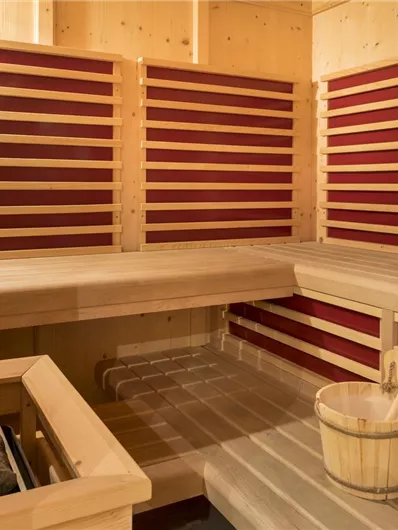 Een lichte sauna met houten banken en rode accenten. In de ruimte staan een emmer en een opscheplepel klaar.