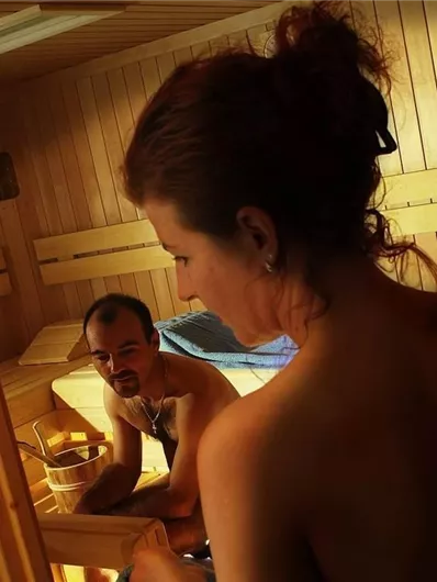 Een ontspannen saunagebied met twee personen. De warme houtafwerking en het zachte licht creëren een rustgevende sfeer.