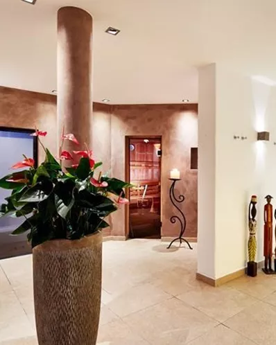 Ein modernes Wellnesscenter mit einem stilvollen Eingangsbereich. Im Hintergrund sind eine Sauna und frische Pflanzen zu sehen.