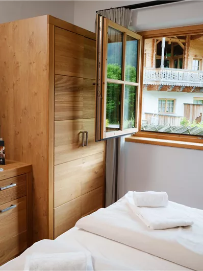 Ein helles Schlafzimmer mit zwei Betten und Holzmöbeln. Das Fenster bietet einen Blick auf eine grüne Landschaft und ein angrenzendes Haus.