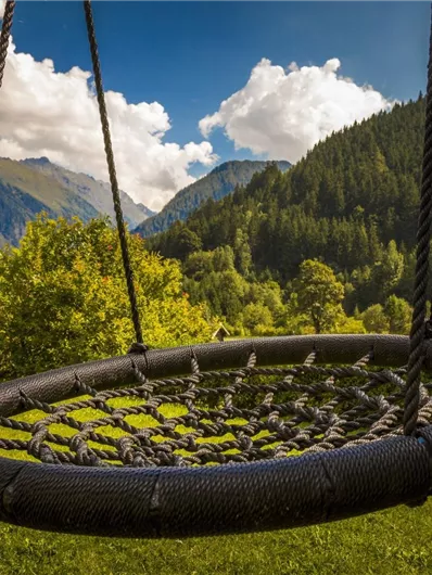 Een schommel in een mooie tuin met bergen op de achtergrond. De wolken aan de blauwe lucht geven de scène een ontspannen sfeer.