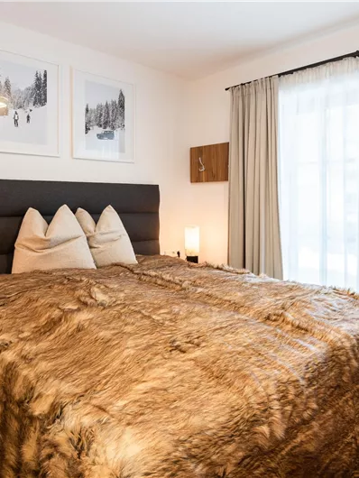 Ein stilvolles Schlafzimmer mit einem großen Bett und gemütlicher Bettwäsche. Fenster mit Vorhängen lassen viel Tageslicht herein.