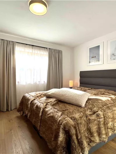 Ein helles Schlafzimmer mit einem großen Bett und Holzfußboden. Die Wände sind mit Bildern und eleganten Vorhängen dekoriert.