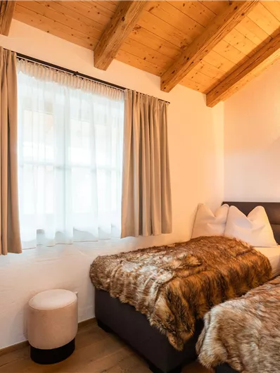 Ein gemütliches Schlafzimmer mit zwei Betten und einem Holzdach. Die Fenster lassen viel Licht hinein und die Vorhänge sind in sanften Farbtönen gehalten.