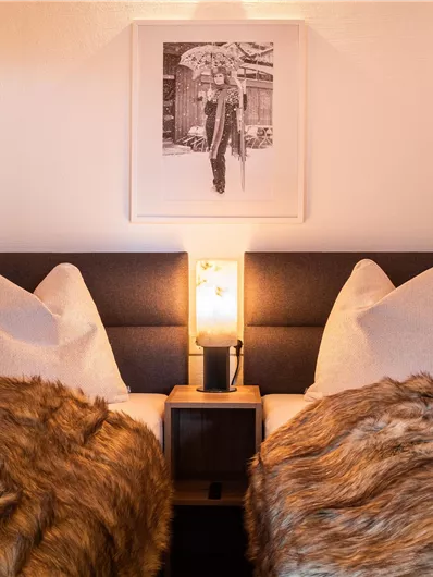 Ein gemütliches Schlafzimmer mit zwei Betten und Kissen. Eine warme Lichtquelle sorgt für eine einladende Atmosphäre.