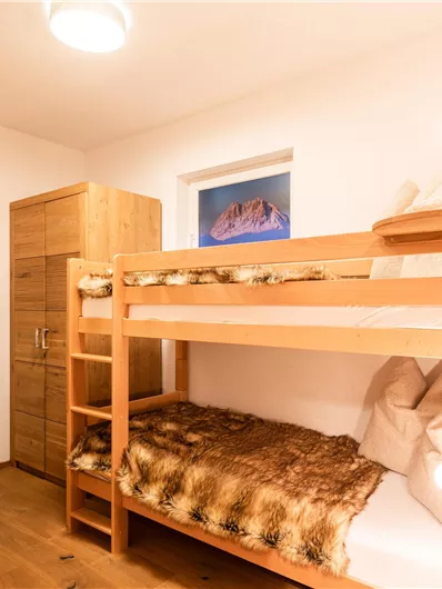 Ein gemütliches Zimmer mit einem Etagenbett aus Holz. An der Wand hängen ein paar Kleiderhaken und es gibt eine Kommode.