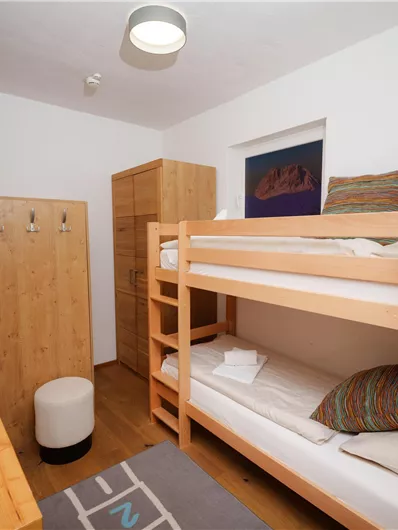 Ein einfaches Schlafzimmer mit einem Etagenbett und einem Schreibtisch. An der Wand hängt eine Plüschgiraffe und es gibt einen Holzschrank.