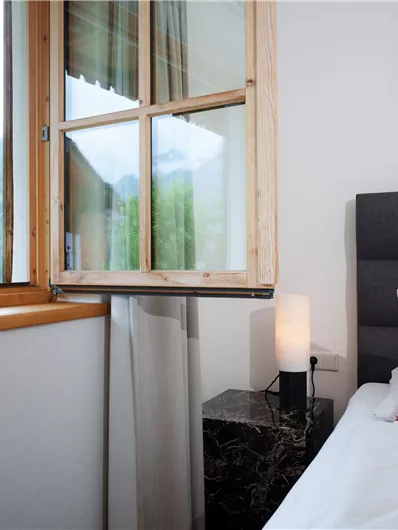 Ein gemütliches Schlafzimmer mit einem Fenster, das auf die Berge zeigt. Auf dem Bett liegt ein Kissen mit einem ansprechenden Muster.