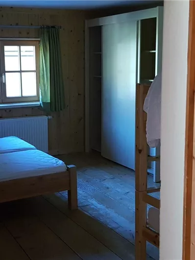 Ein einfaches Zimmer mit zwei Einzelbetten und einem Fenster. Die Wände sind aus Holz und es gibt einen Schrank.