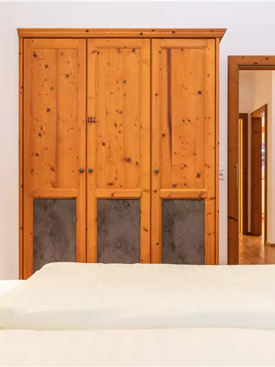 Ein gemütliches Schlafzimmer mit einem Holzschrank und einem offenen Türbereich. Das Bett ist einladend mit weißen Kissen und Bettwäsche.