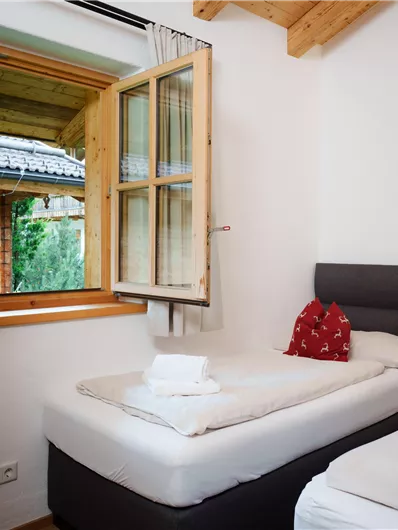 Ein helles Zimmer mit zwei Betten und einem offenen Fenster. Der Blick zeigt eine schöne Landschaft mit holzverkleideten Wänden.