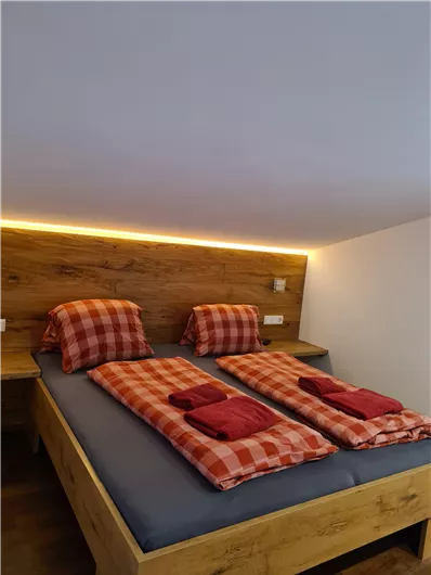 A cozy bedroom with a wooden bed and red checkered bedding. The soft lighting creates a pleasant atmosphere.