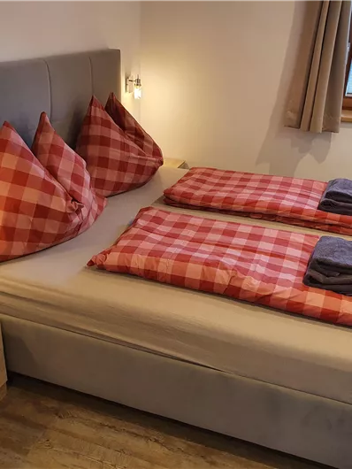 A cozy bedroom with a double bed and checkered pillows. The wooden details and the large window create an inviting atmosphere.