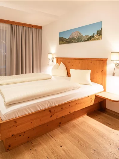Ein gemütliches Schlafzimmer mit einem Doppelbett und hellen Holzdetails. Der Raum ist lichtdurchflutet und hat große Fenster mit Vorhängen.
