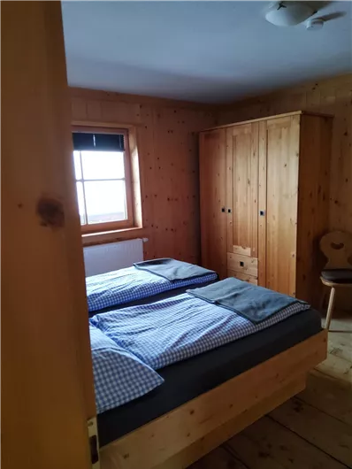 Ein gemütliches Schlafzimmer mit zwei Betten und Holzmöbeln. Das Zimmer hat eine Fensteransicht und eine warme, einladende Atmosphäre.