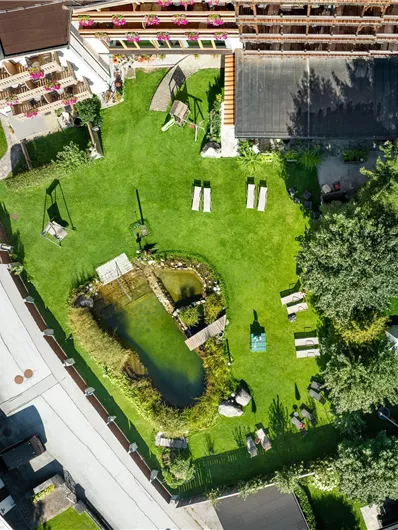 Een groene tuinenlandschap met een vijver in het midden. Omgeven door gezellige ligstoelen en bomen.
