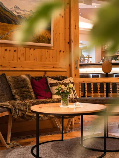 Een gezellige woonkamer met houten wandbekleding en een ronde salontafel. Op de bank liggen kussens, en een bos bloemen staat op de tafel.