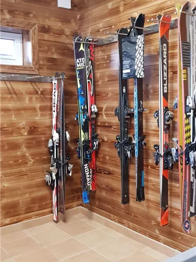 Ein Skiraum mit mehreren Skiern, die an einer Holzwand hängen. Der Boden ist gefliest und die Atmosphäre ist gemütlich.