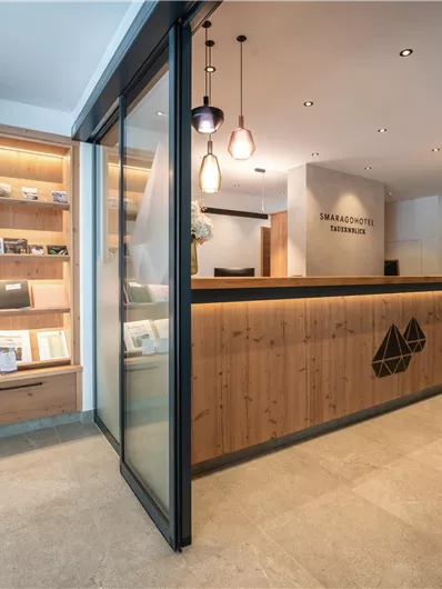 Een moderne receptiehal met een houten balie en elegante verlichting. Op de achtergrond zijn brochures en een grote klok zichtbaar.