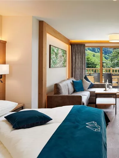 Een moderne hotelkamer met houten wanden en een balkon. De inrichting is eenvoudig en gezellig met een comfortabel bed en een zithoek.