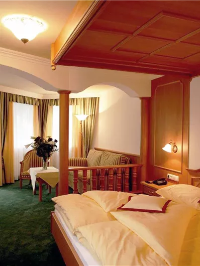 Een gezellig hotelkamer met een groot bed en een zithoek. De ramen zijn gedecoreerd met gordijnen en de kamer heeft een elegante houten stijl.