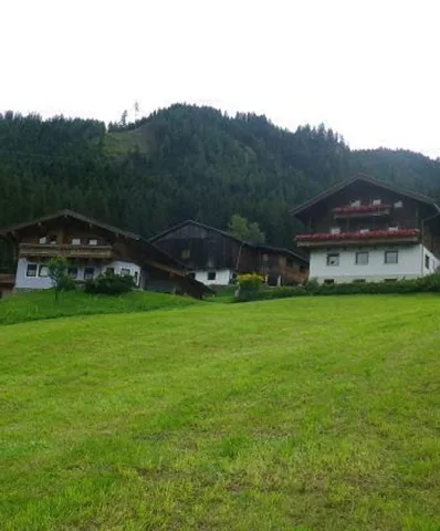 Eine ruhige Landschaft mit grünen Wiesen und mehreren traditionellen Gebäuden. Im Hintergrund erhebt sich ein bewaldeter Hügel.