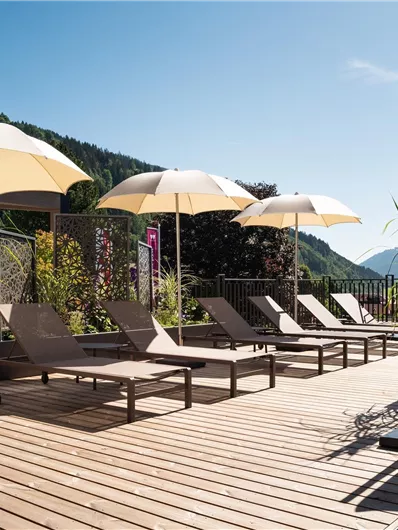 Ein schöner Außenbereich mit Liegen und Sonnenschirmen. Die Umgebung ist grün und bietet einen herrlichen Blick auf die Berge.