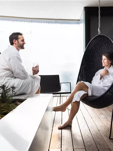 A relaxing place with two people in bathrobes sitting in modern hanging chairs. The atmosphere is calm and inviting, surrounded by subtle nature design.