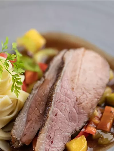 Ein elegant angerichteter Teller mit zartem Fleisch, frischem Gemüse und einer Portion Pasta. Die Farben sind lebhaft und die Anrichtung ist ansprechend.
